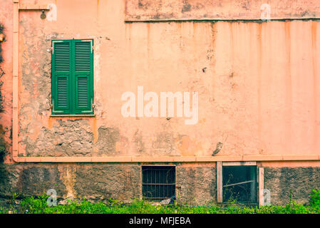 Small window with closed green shutters on an old and weathered empty pastel pink wall Stock Photo