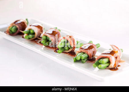 Green bean bundles wrapped in bacon on a white plate. Stock Photo