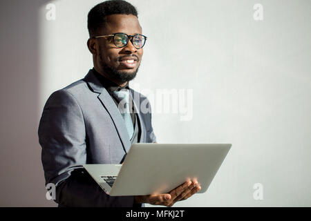 Dark skinned coworker wearing glasses and using laptop in office Stock Photo
