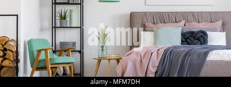 Cozy, scandinavian bedroom interior for a woman with a mint armchair, wooden decoration, bookshelf, plants and cushions on a big bed Stock Photo