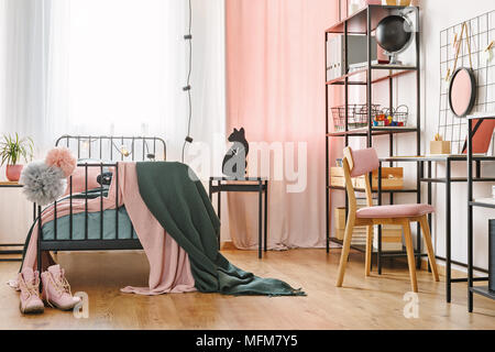 Industrial black furniture and cute pink textiles in a teenage student's modern bedroom interior with cozy metal frame bed and workspace Stock Photo