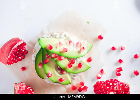 Crisp bread healthy snack with avocado slices, soft cottage cheese and pomegranate seeds. Easy breakfast concept on a white background with copy space Stock Photo