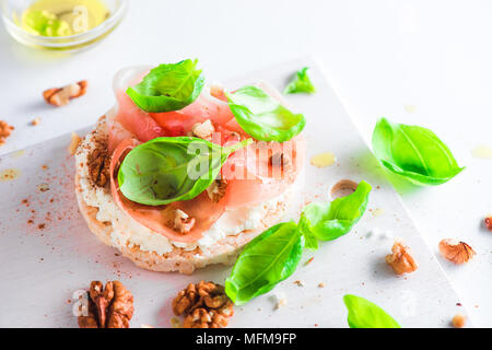 Crisp bread healthy snack with Parma ham, soft cottage cheese, walnuts, olive oil, paprika, fresh basil leaves. Easy breakfast close-up on a white bac Stock Photo