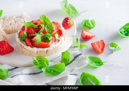 Healthy snack with crisp bread, fresh strawberries, goat cheese, and basil leaves. Easy breakfast close-up on a white background with copy space. Stock Photo