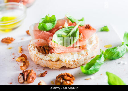 Crisp bread healthy snack with Parma ham, soft creme cheese, olive oil, fresh basil leaves, walnuts. Easy breakfast close-up on a white background wit Stock Photo