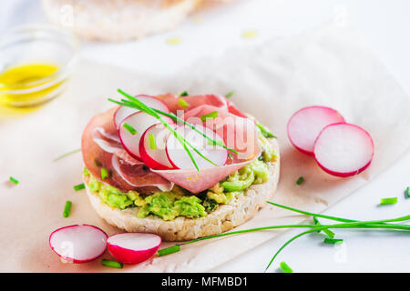 Crisp bread healthy snack with Parma ham, avocado spread, radish slices, scallion, olive oil. Easy breakfast close-up on a white background with copy  Stock Photo