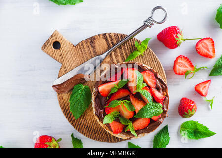 Crisp bread healthy snack with fresh strawberries, chocolate spread, mint leaves on a round cutting board with a dessert knife. Easy breakfast close-u Stock Photo