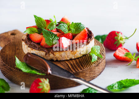 Crisp bread healthy snack with fresh strawberries, chocolate spread, mint leaves on a round cutting board with a dessert knife. Easy breakfast close-u Stock Photo