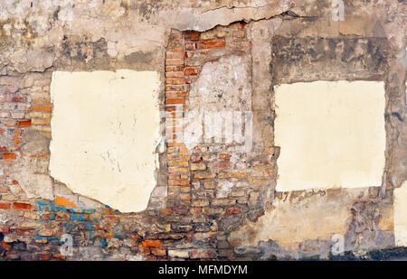 A piece of the wall of the ruined house with paint stains and yellow plaster patches that close the windows. Old ruined city abstract background Stock Photo
