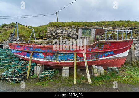 An old abandoned Fishing Boat in need of repair stands propped up against the Castle Walls of Slade Fishing Village in County Wexford, Eire. Stock Photo