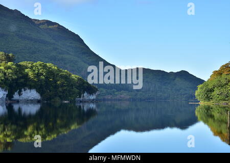 Reflections of hills forests and rock formations on calm surface of Muckross Lake in Ireland. Stock Photo