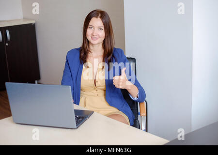Cheerful office-worker showing thumbs up in front of laptop. Stock Photo