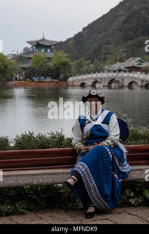 Lijiang, China - March 23, 2018: Chinese woman wearing a traditional Bai minority attire sitting in front of the Black Dragon Pool in Lijiang Stock Photo