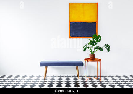 Monstera plant on an orange side table in a minimalist, white apartment interior with colorful elements and gallery Stock Photo