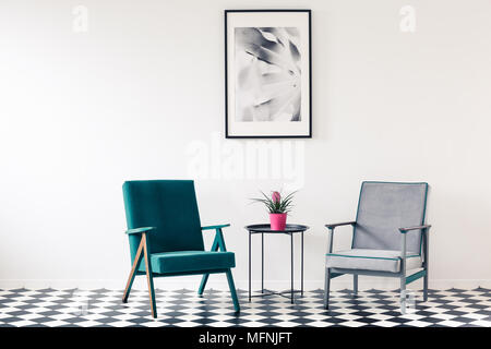 Framed photography mock-up on a white, empty wall above retro armchairs in a minimalist living room interior with checkered floor Stock Photo