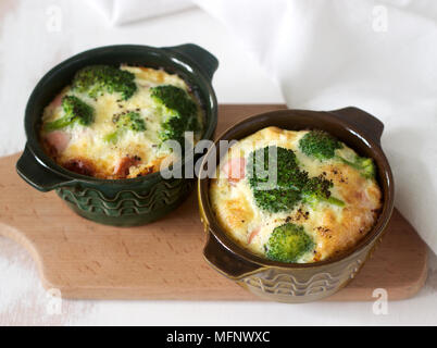 Baked scrambled eggs with broccoli, sausages and cheese served with slices of bread. Rustic style, selective focus. Stock Photo