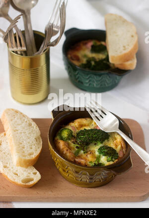 Baked scrambled eggs with broccoli, sausages and cheese served with slices of bread. Rustic style, selective focus. Stock Photo