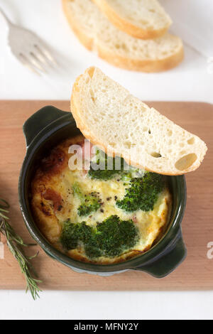 Baked scrambled eggs with broccoli, sausages and cheese served with slices of bread. Rustic style, selective focus. Stock Photo