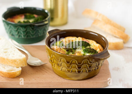 Baked scrambled eggs with broccoli, sausages and cheese served with slices of bread. Rustic style, selective focus. Stock Photo