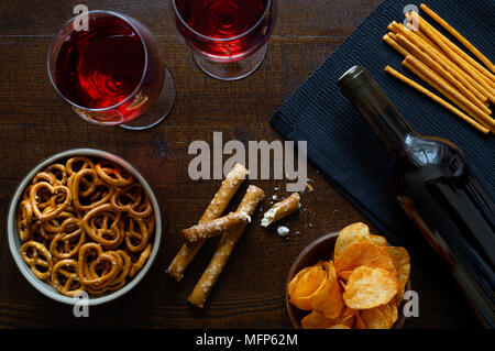 Red wine with savoury party snacks on rustic dark wood background from above. Stock Photo