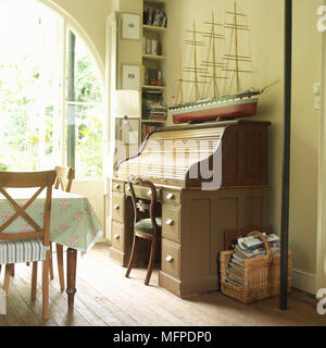 A traditional, roll top writing desk, model ship, and wooden table by a sunny window. Stock Photo