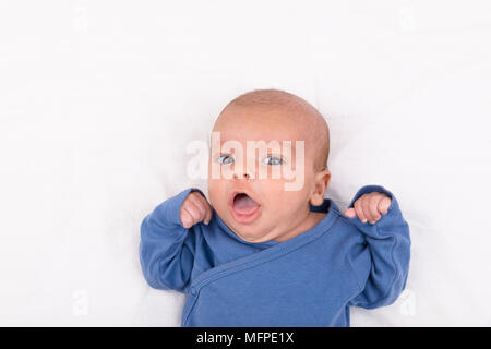 Cute eurasian newborn baby boy wearing a blue infant bodysuit on white sheet and looking at the camera, with copy space Stock Photo