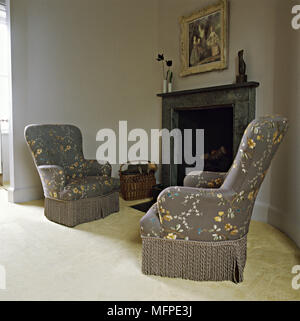 Pair of old fashioned armchairs with floral pattern fabric in front of fireplace Stock Photo