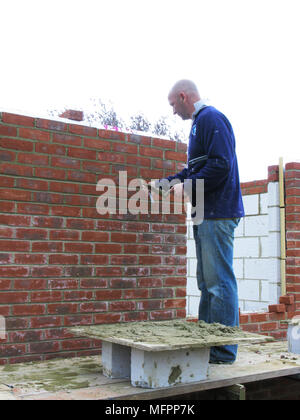 Builder / construction worker building a brick wall cementing bricks in on an extension or new property model release Stock Photo