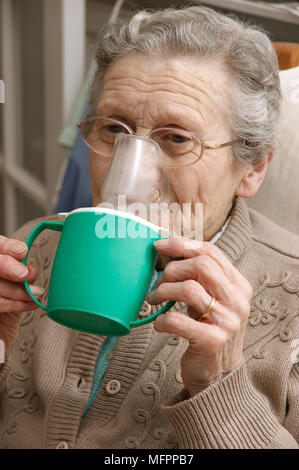 Elderly woman using a steam inhaler inhaling a decongestant for colds & bronchitis model release Stock Photo