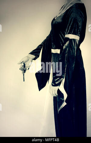 a woman in Victorian dress holding a crucifix in her hands Stock Photo