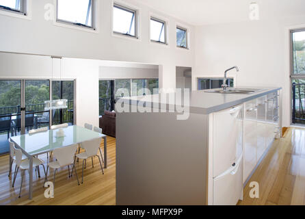 Sink set in central island unit in modern kitchen with view to dining table and chairs below Stock Photo