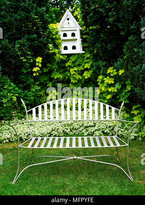 Backyard detail with a metal bench seat, shrubbery, and a white bird house. Stock Photo