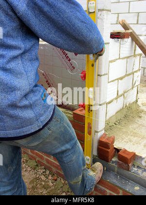 Builder / construction worker using a spirit level building a brick wall showing celotex thermal insulation board & cavity walls in an extension or ne Stock Photo