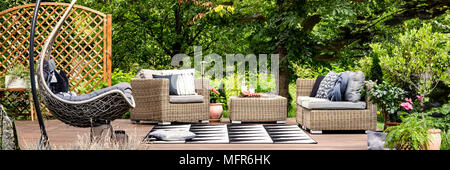 Picnic food and cold lemonade in glass carafe placed on a garden table standing on a terrace with hammock chair Stock Photo
