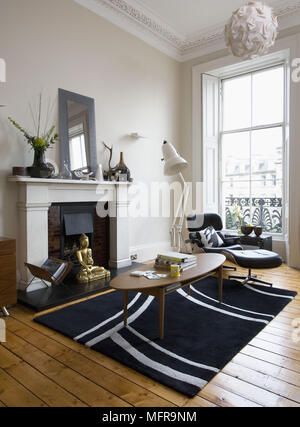 Eames lounge chair and ottoman next to oval coffee able in front of fireplace in contemporary sitting room Stock Photo