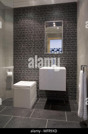 Mirror above wall mounted washbasin next to square toilet in recessed area of bathroom Stock Photo