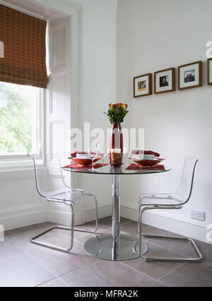 Pair of transparent plastic and steel chairs at round table set for dinner Stock Photo