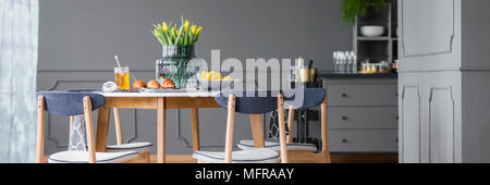 Yellow tulips on wooden dining table with chairs in grey, rustic dining room interior Stock Photo