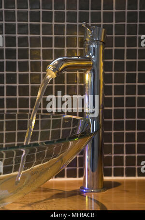 Water running from chrome tap into modern glass washbasin Stock Photo