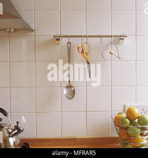 Cooking utensils hanging from steel hooks on white tiled wall Stock Photo