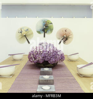 Wooden dining table set with bowls and chop sticks and flower arrangement of pink hydrangeas Stock Photo