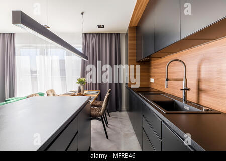 Kitchen interior with black cabinets, steel tap and wooden table in dining area Stock Photo