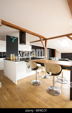 White, modern kitchen interior with bar stools, black table and wooden floor
