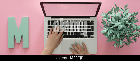Freelancer working on a laptop in a modern, pink workspace with a mint plant Stock Photo