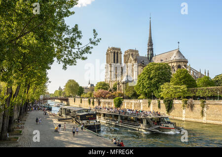 Parisians and tourists make the most of springtime to take a trip on a riverboat or stroll along the Seine in front of Notre-Dame de Paris cathedral. Stock Photo