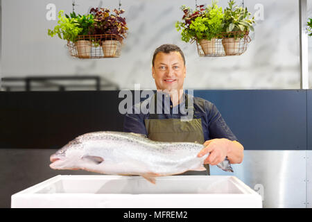 happy male seller holding trout at fish shop Stock Photo