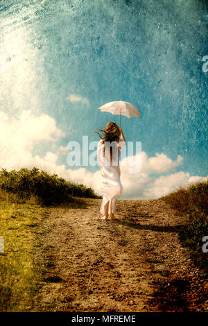 a girl in a white dress is walking in the dunes with a parasol Stock Photo