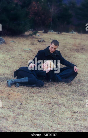 a couple in black clothes is lying on a meadow in winter Stock Photo
