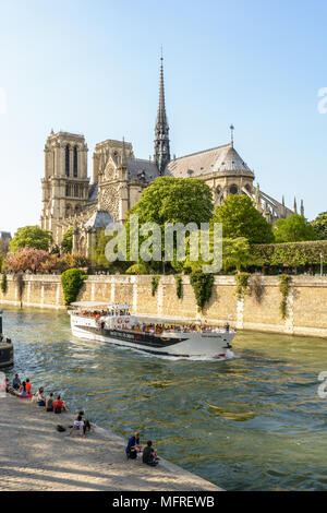 Parisians and tourists make the most of springtime to take a trip on a river boat or relax beside the Seine in front of Notre-Dame de Paris cathedral. Stock Photo