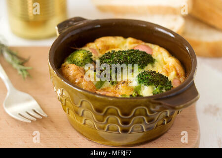 Baked scrambled eggs with broccoli, sausages and cheese served with slices of bread. Rustic style, selective focus. Stock Photo